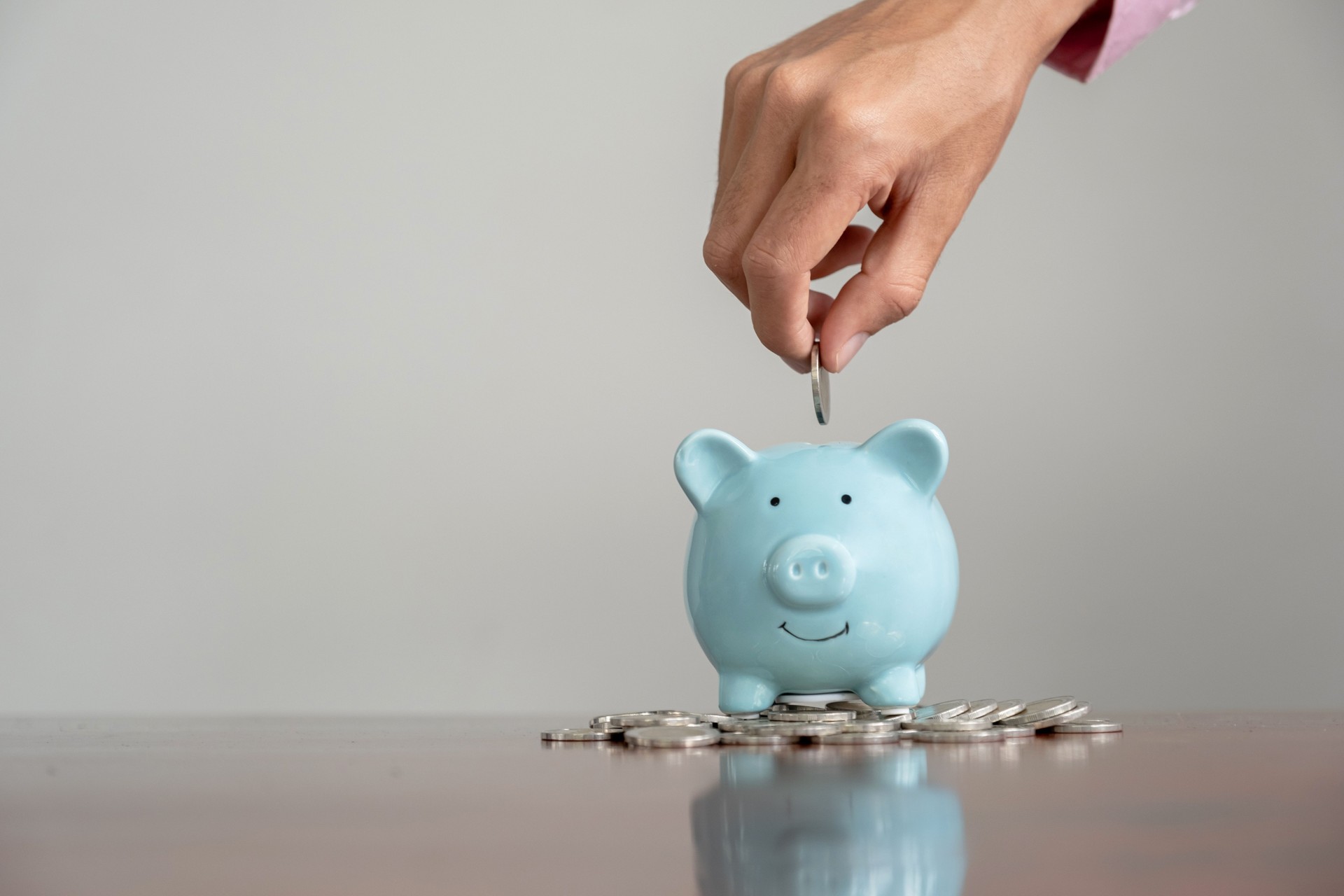 Businessman hand putting coin into blue piggy bank